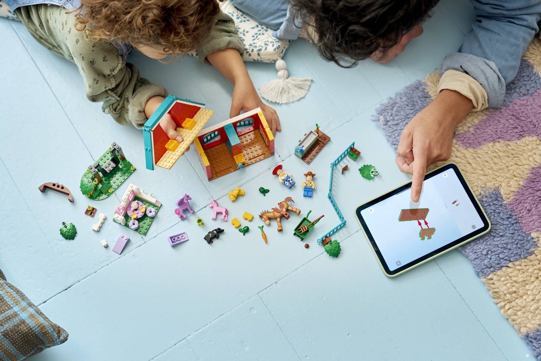 Child and adult lying on the floor using a tablet to build LEGO® ǀ Disney and Pixar Toy Story 5 Blaze’s Horse Ranch.