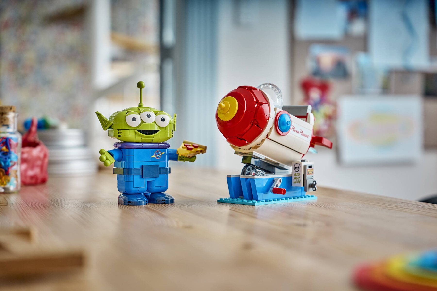 LEGO® | Disney Pixar Alien with Pizza Planet Rocket Ride displayed on a wooden table; alien figure detached from ride.