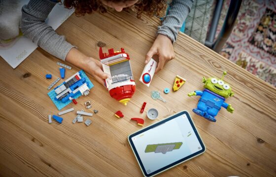 Aerial view of a girl at a table using a tablet to build a LEGO® | Disney Pixar Alien with Pizza Planet Rocket Ride.