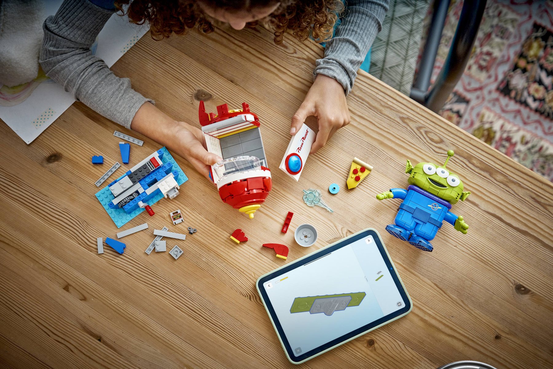 Aerial view of a girl at a table using a tablet to build a LEGO® | Disney Pixar Alien with Pizza Planet Rocket Ride.