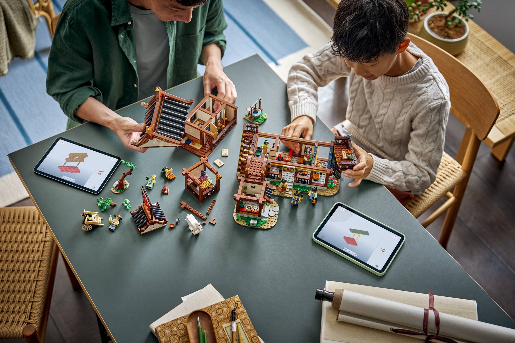 A man and a boy sitting at a table, using tablets to build a LEGO® Chinese Festivals Ancient Moon-Gazing Inn together.