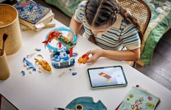 A girl holding a brick-built fish while using a tablet to build a LEGO® Chinese Festivals Prosperity Carp Leaping set.