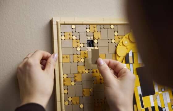Close-up of a woman preparing to place a part over the hanging mechanism of a LEGO Art Gustav Klimt – The Kiss.