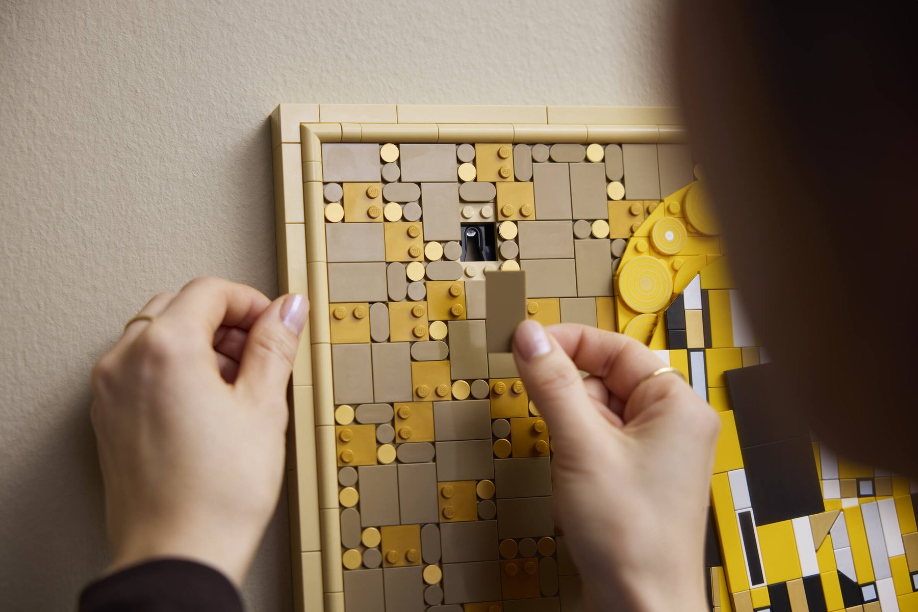 Close-up of a woman preparing to place a part over the hanging mechanism of a LEGO Art Gustav Klimt – The Kiss.