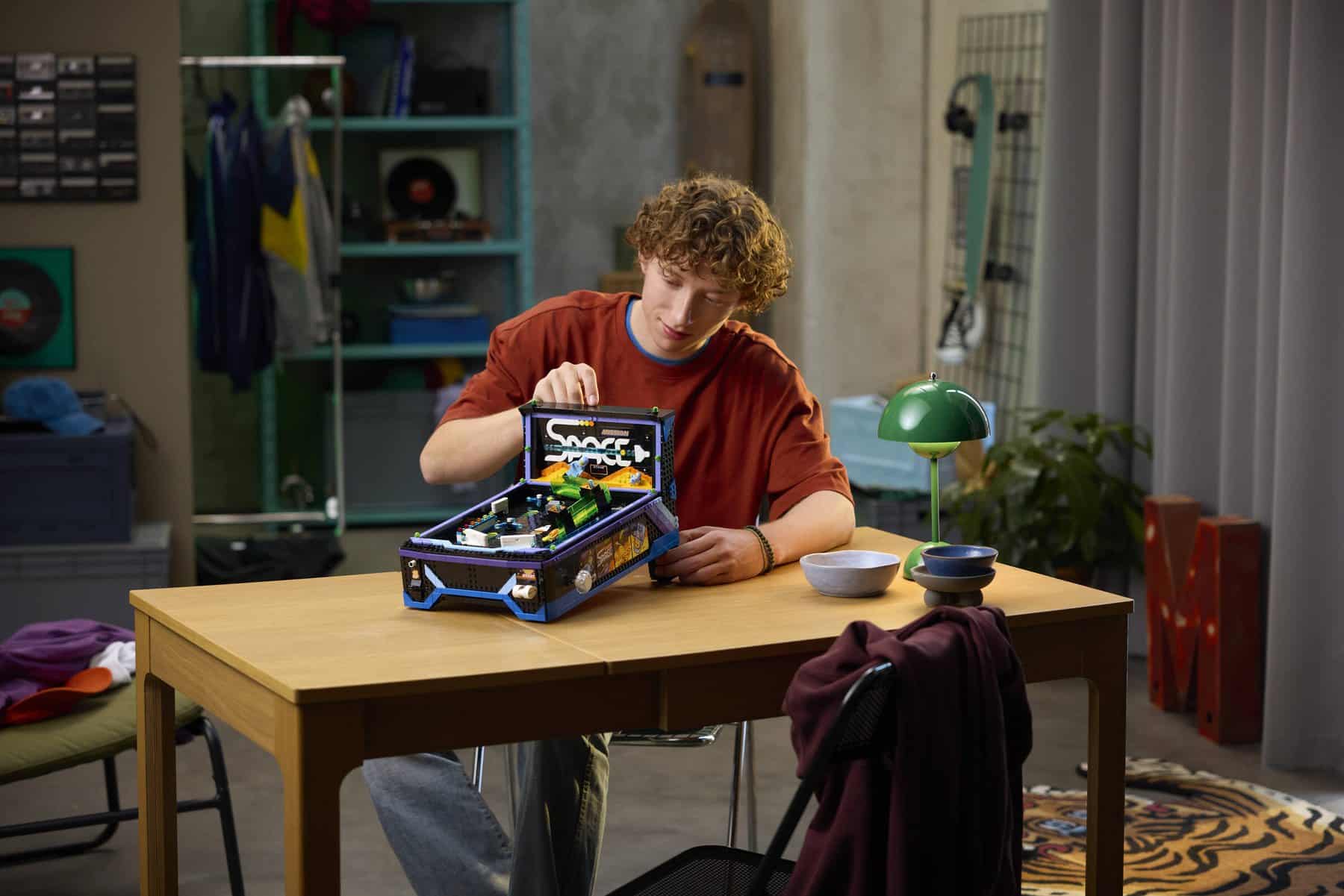 A man sitting at a table adjusting an assembled LEGO® Icons Arcade Pinball Machine set.