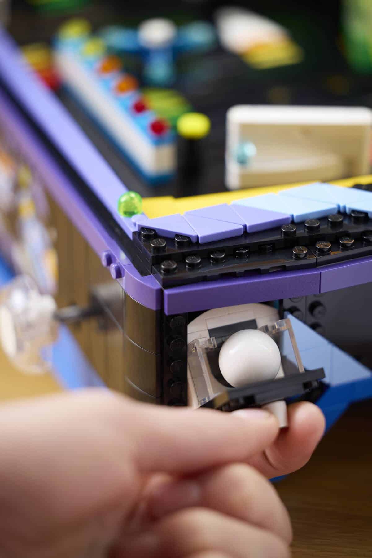 A hand loading a pinball into a LEGO® Icons Arcade Pinball Machine set.