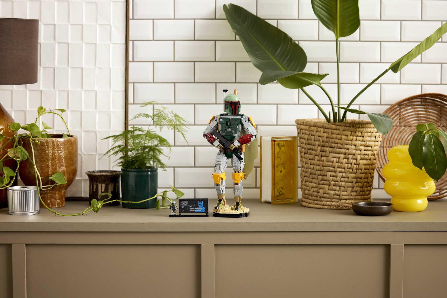 Built LEGO® Star Wars™ Boba Fett and info plaque with minifigure displayed on a sideboard beside two potted plants.