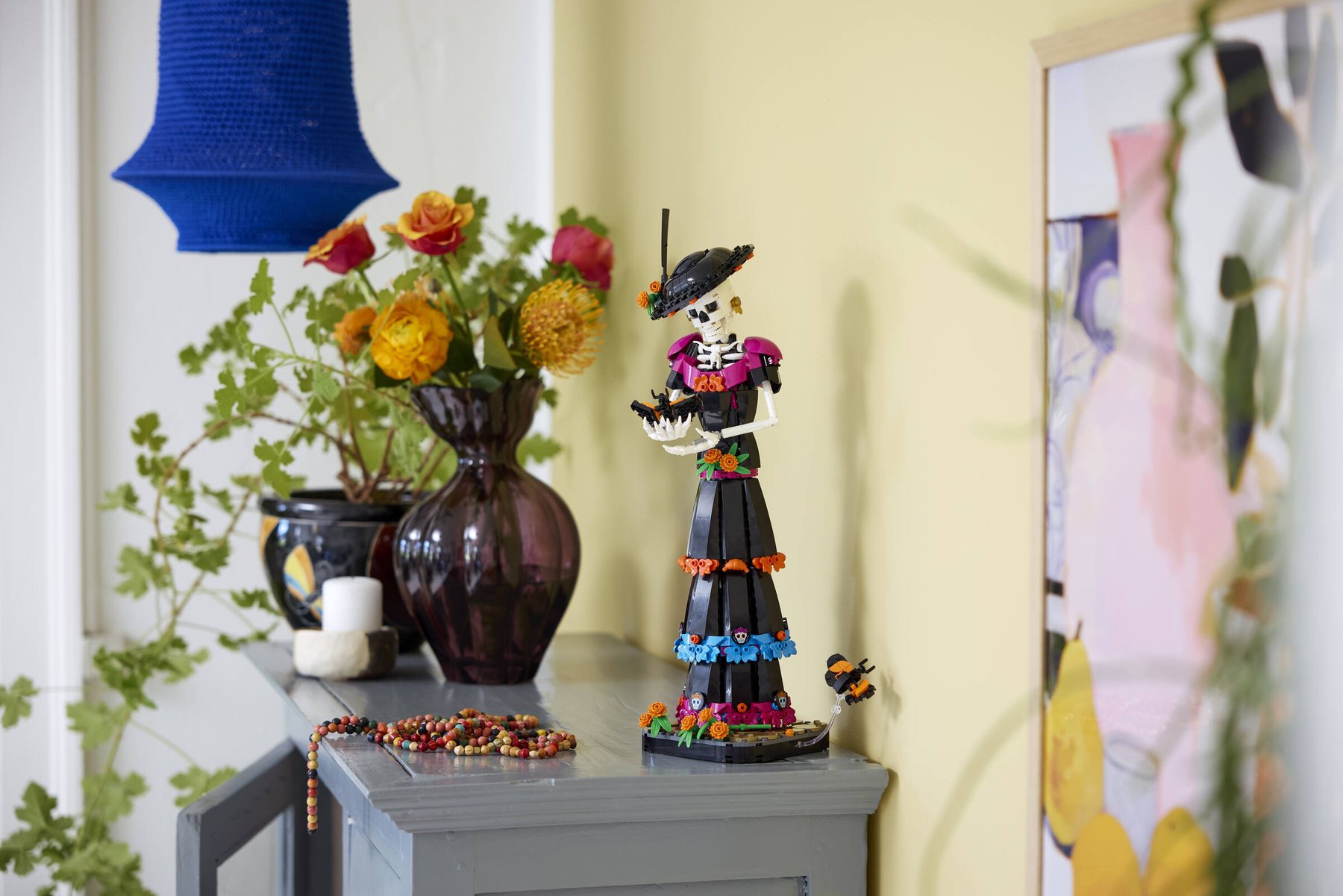LEGO® Ideas La Catrina set showing a skeleton figure holding a brick-built butterfly, displayed on a sideboard.
