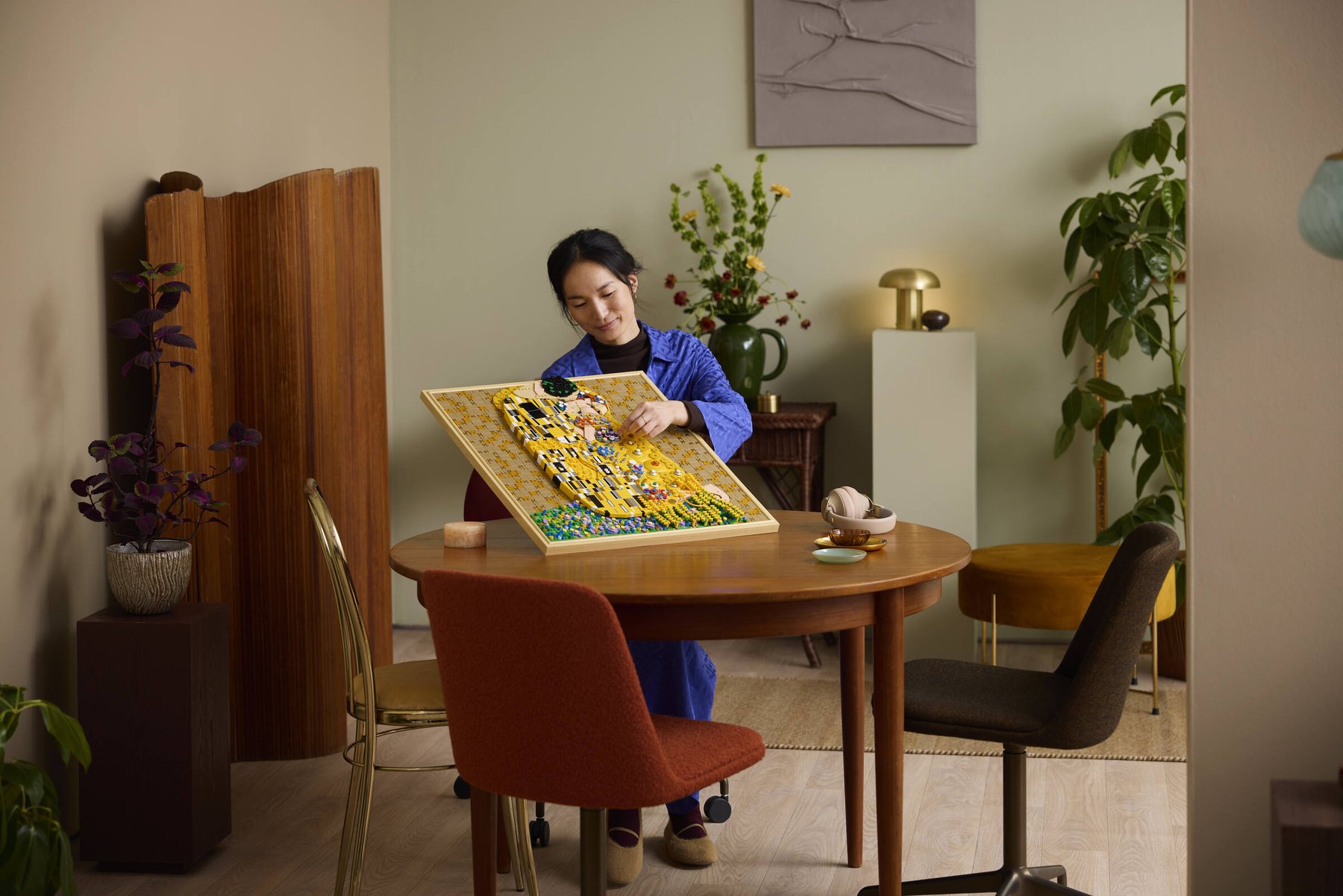 Woman at a table adjusting parts of a built LEGO® Art Gustav Klimt – The Kiss set.