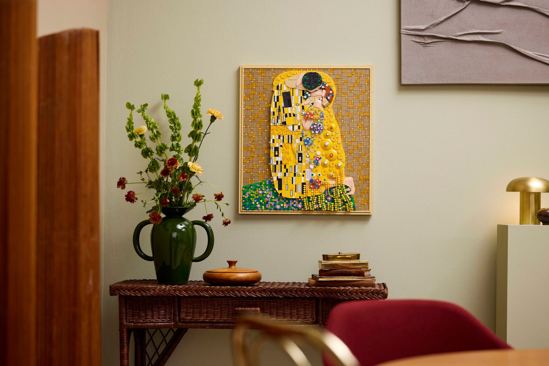 LEGO® Art Gustav Klimt – The Kiss shown hanging from a wall above a wicker sideboard with various personal items on it.