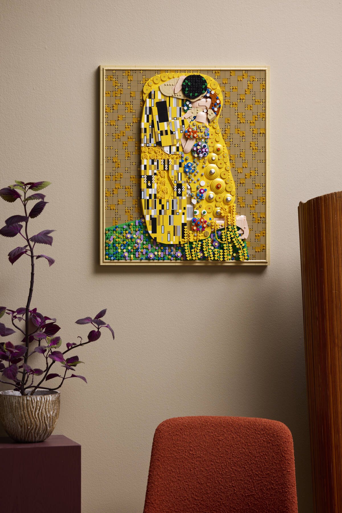 LEGO® Art Gustav Klimt – The Kiss shown hanging from a wall beside a purple and green houseplant.
