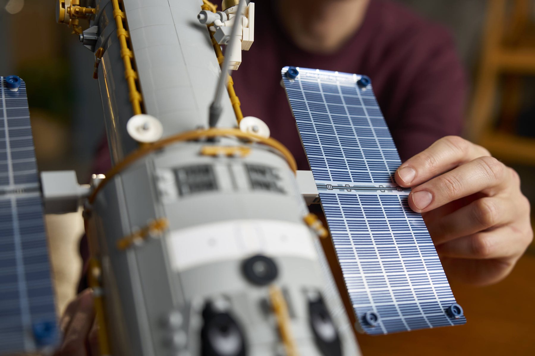 Close-up of a man adjusting one of the solar arrays on a LEGO® Icons Hubble Space Telescope set.