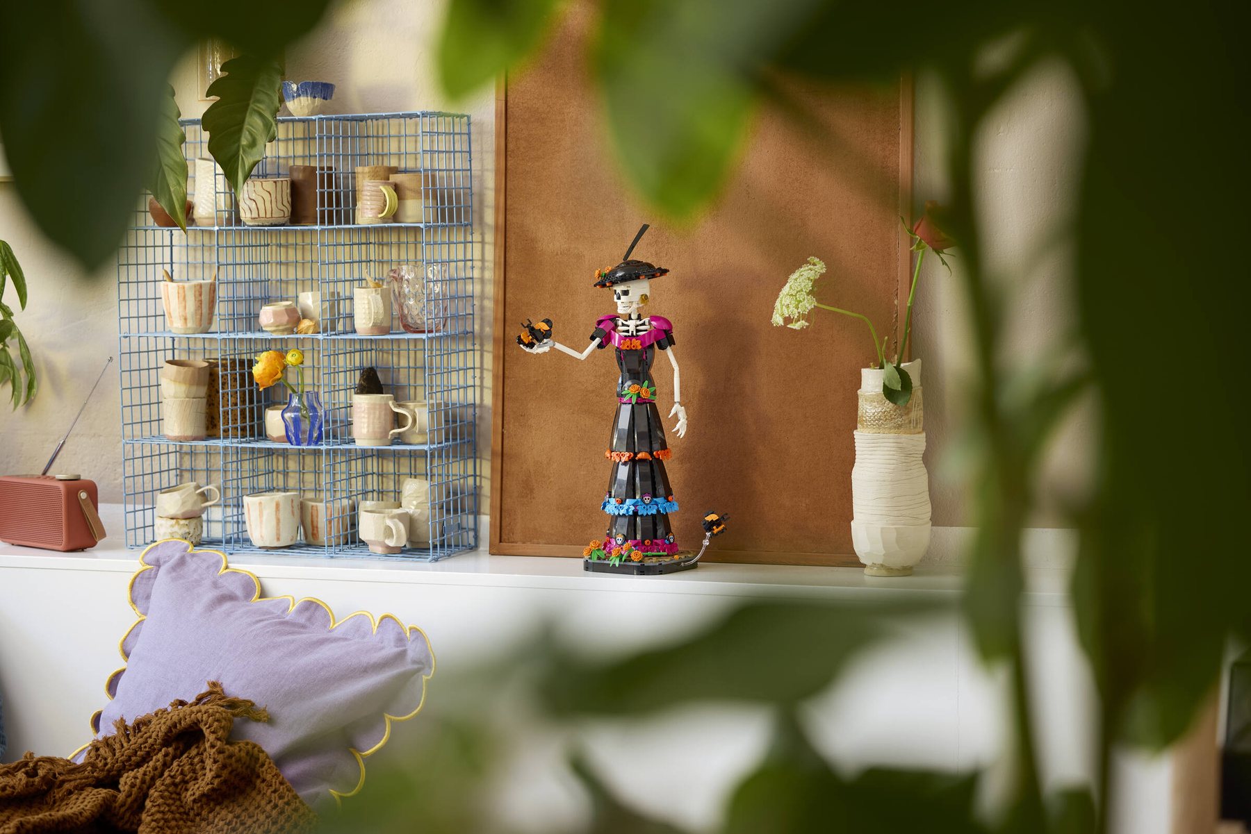 LEGO® Ideas La Catrina set showing a skeleton figure holding a marigold flower, displayed on a chest of drawers.