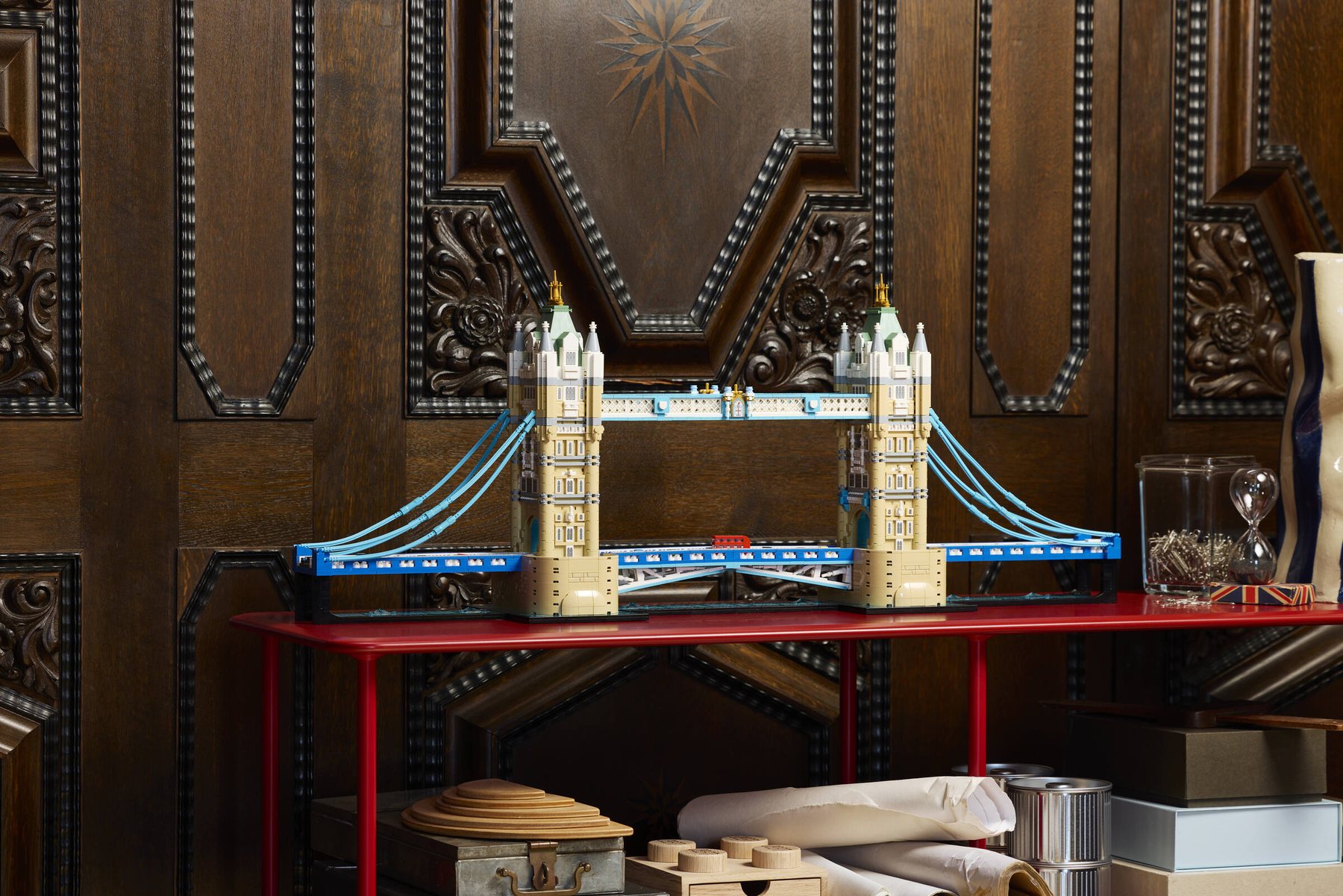 LEGO® Architecture Tower Bridge set displayed on a red metal table, in front of an ornate wooden wall.