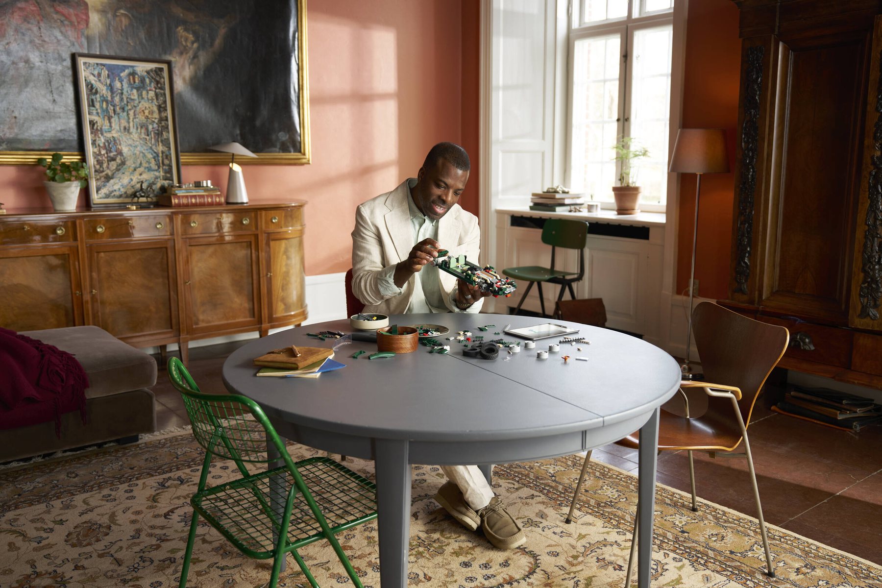 A man sitting at a dining table following instructions on a tablet while building a LEGO® Icons Jaguar E-Type set.