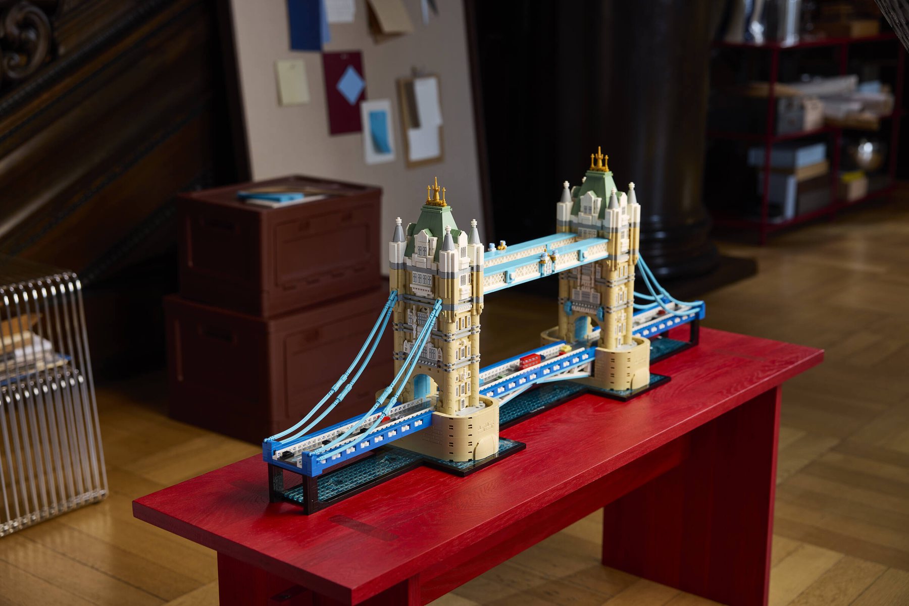 LEGO® Architecture Tower Bridge set displayed on a red metal table, next to wooden boxes and a corkboard.
