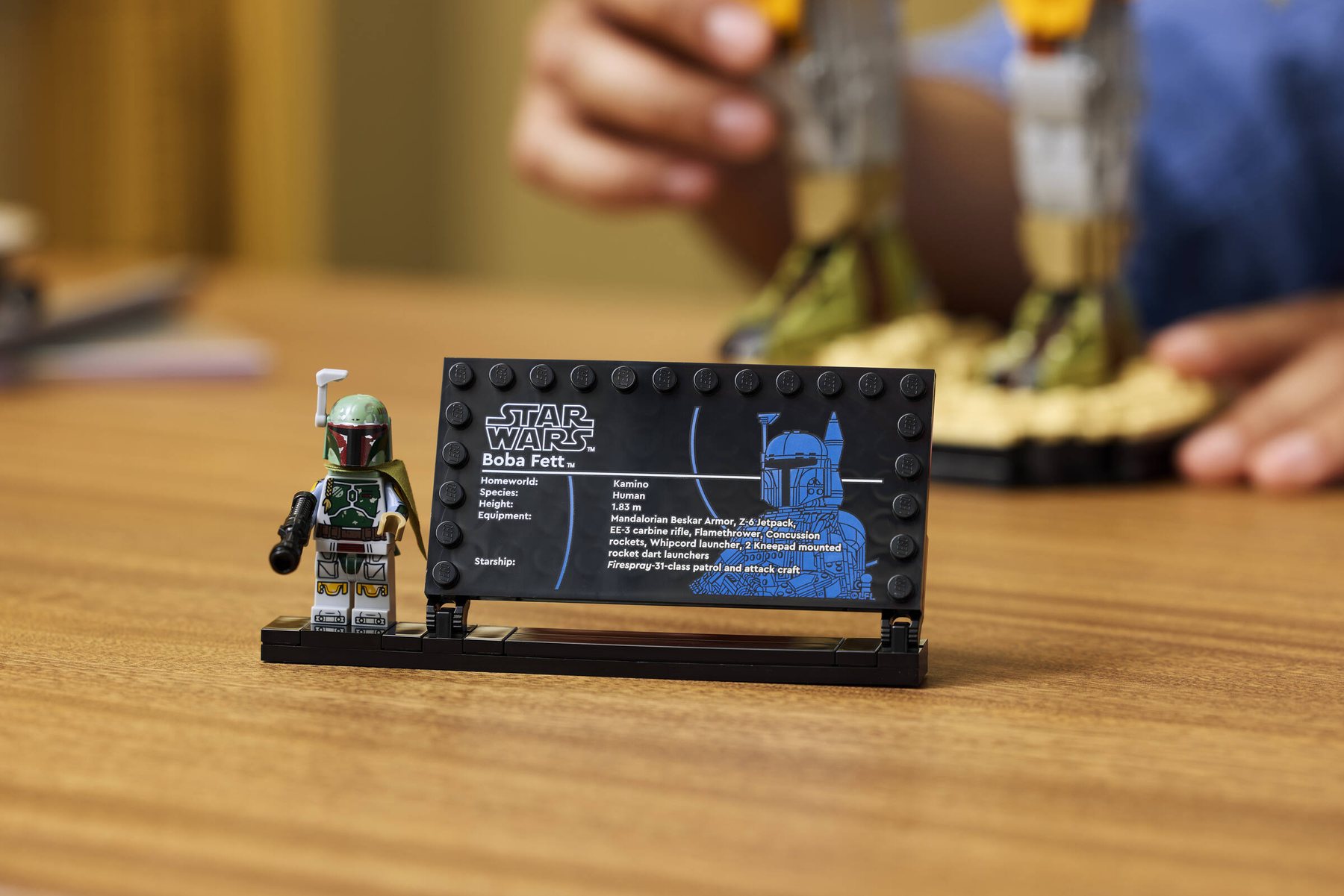 Close-up of the LEGO® Star Wars™ Boba Fett information plaque and minifigure shown on a wooden table.