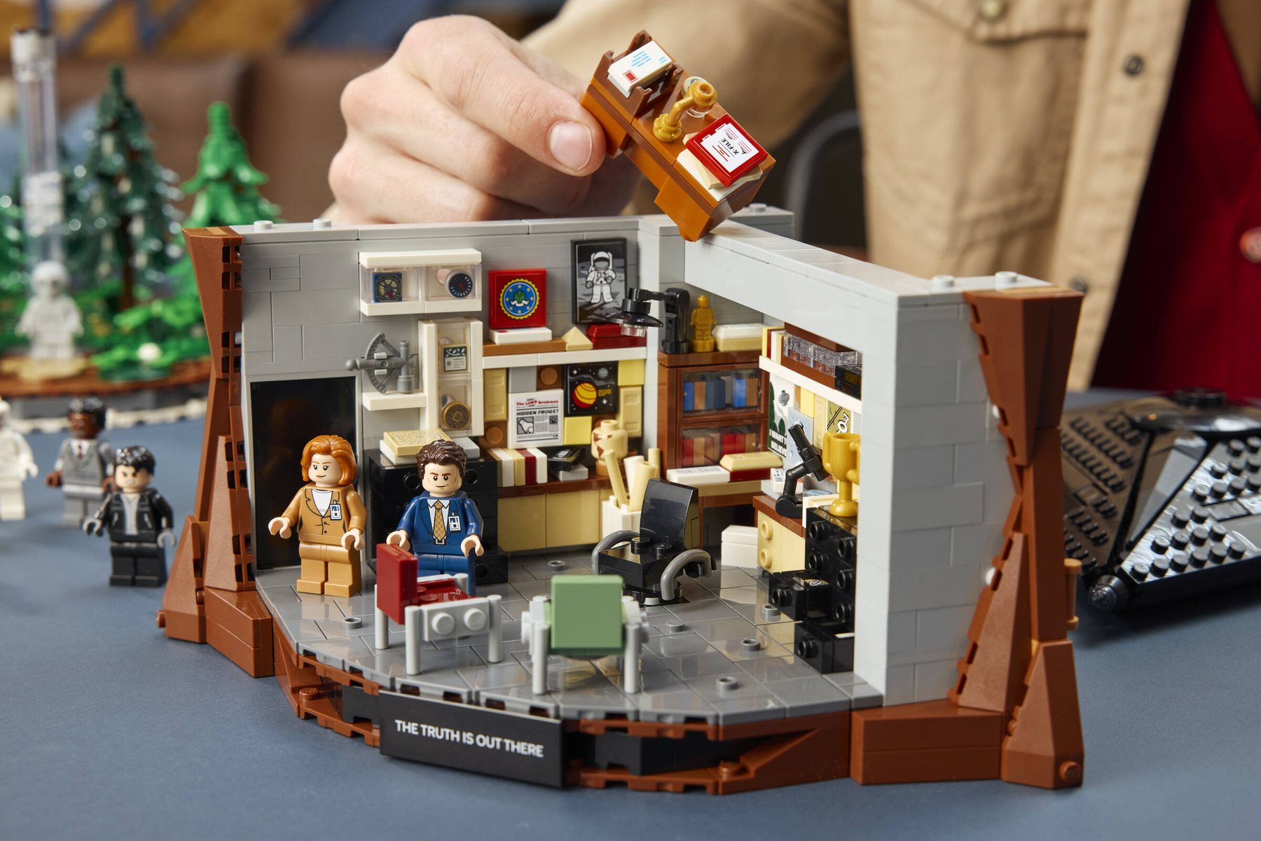 A hand placing a desk part into Fox Mulder’s office in a LEGO® Ideas The X-Files™: THE TRUTH IS OUT THERE set.