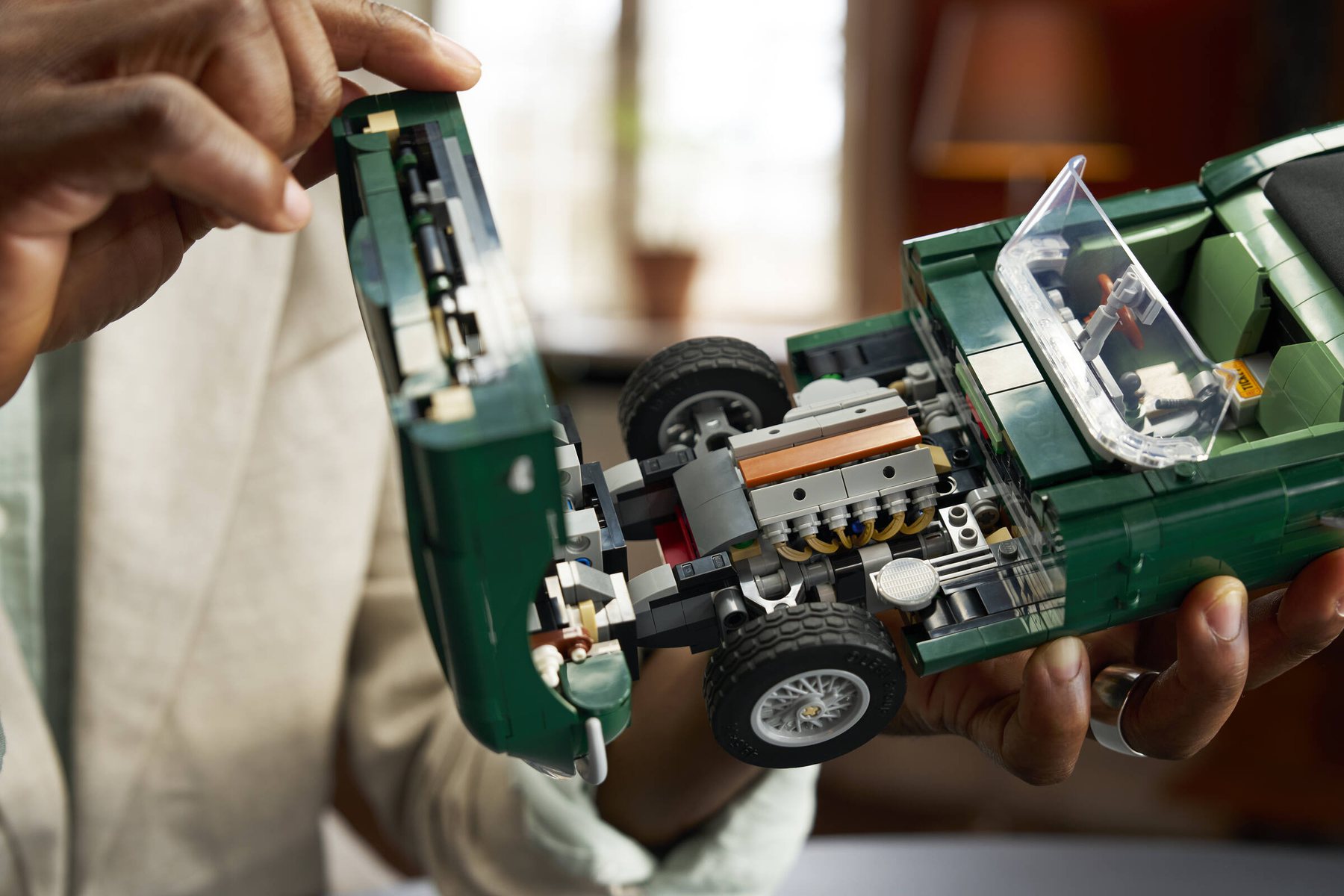 Close-up of a man's hands opening the hood of a LEGO® Icons Jaguar E-Type set, revealing the inline-6 engine inside.