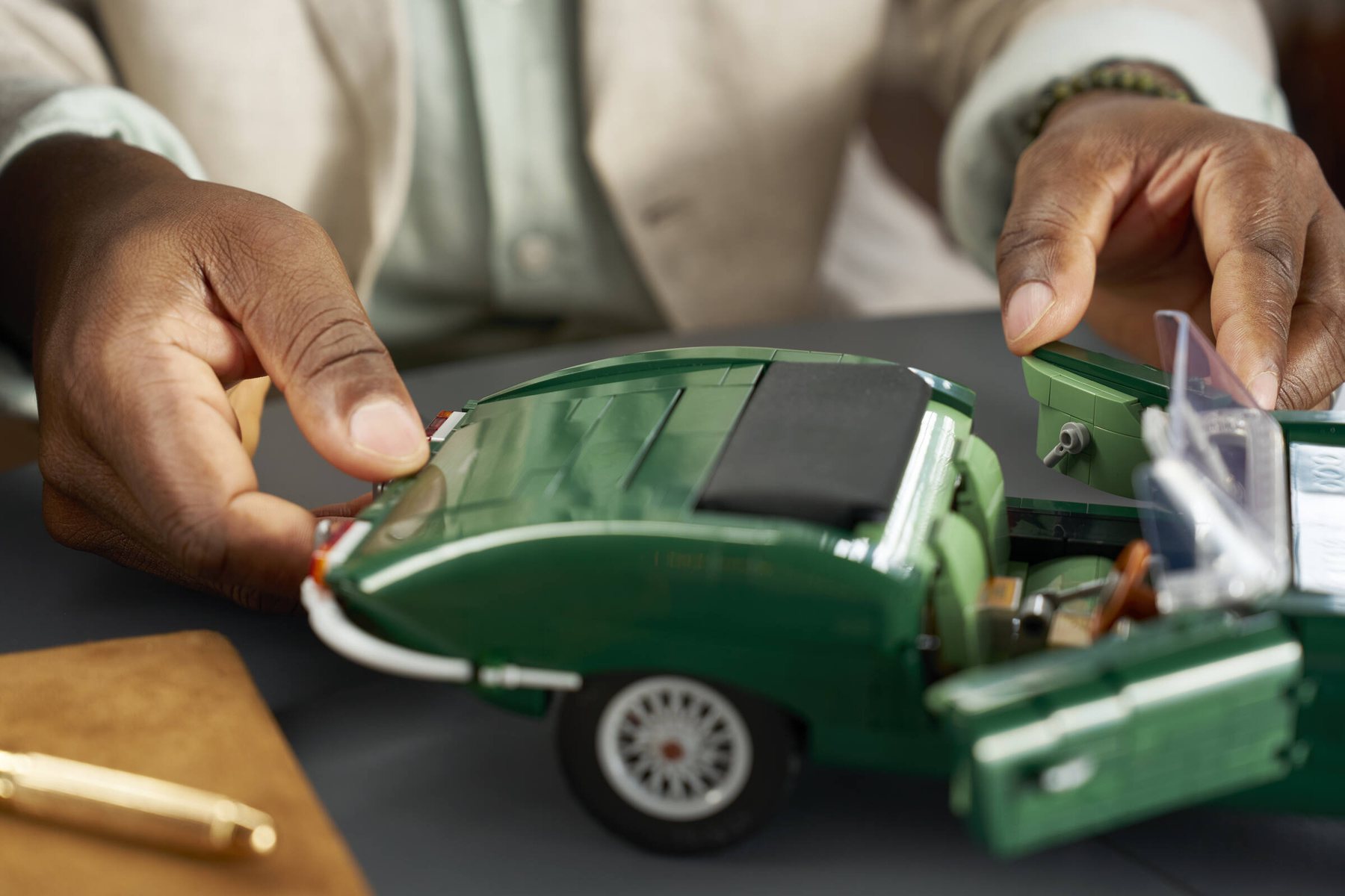 Close-up of a man's hands resting on the trunk and open doors of a LEGO® Icons Jaguar E-Type set.