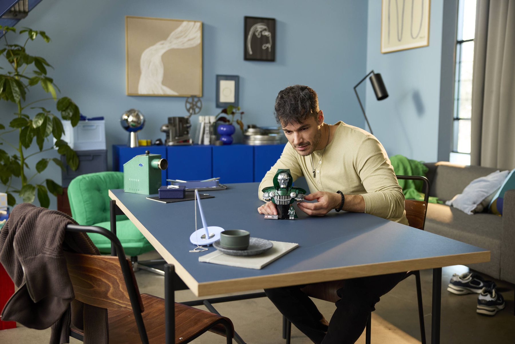 A man sitting at a table adjusting the cape of an assembled LEGO® ǀ Marvel Doctor Doom Bust.