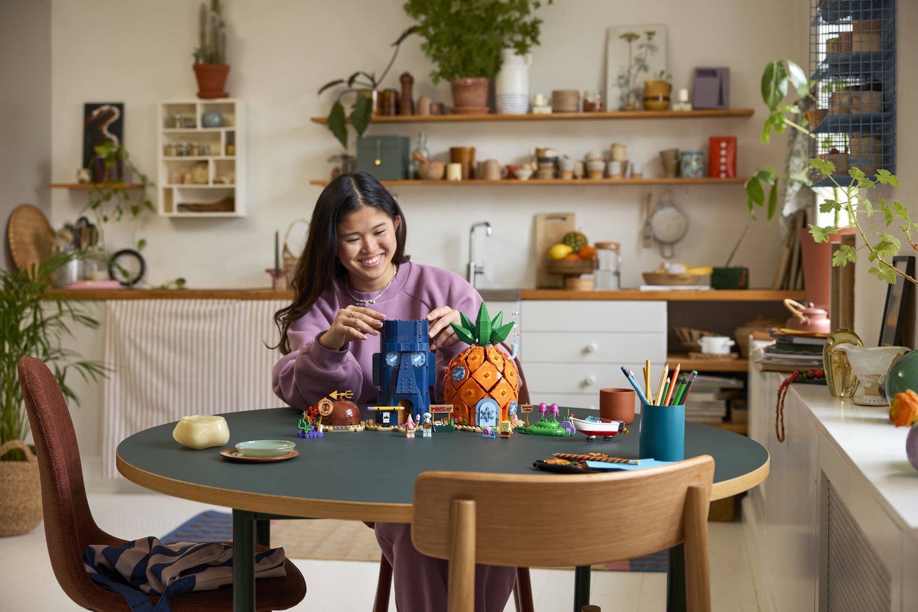 A woman sitting at a table building Squidward Tentacles' house from a LEGO® Icons SpongeBob SquarePants: Bikini Bottom.