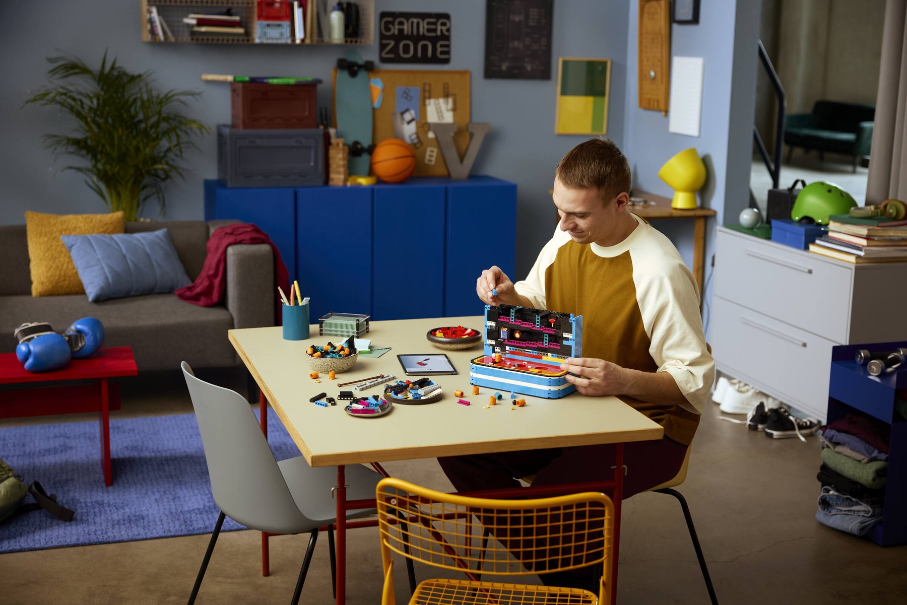 A man sitting at a table following building instructions on a tablet while assembling a LEGO® Donkey Kong™ Arcade set.