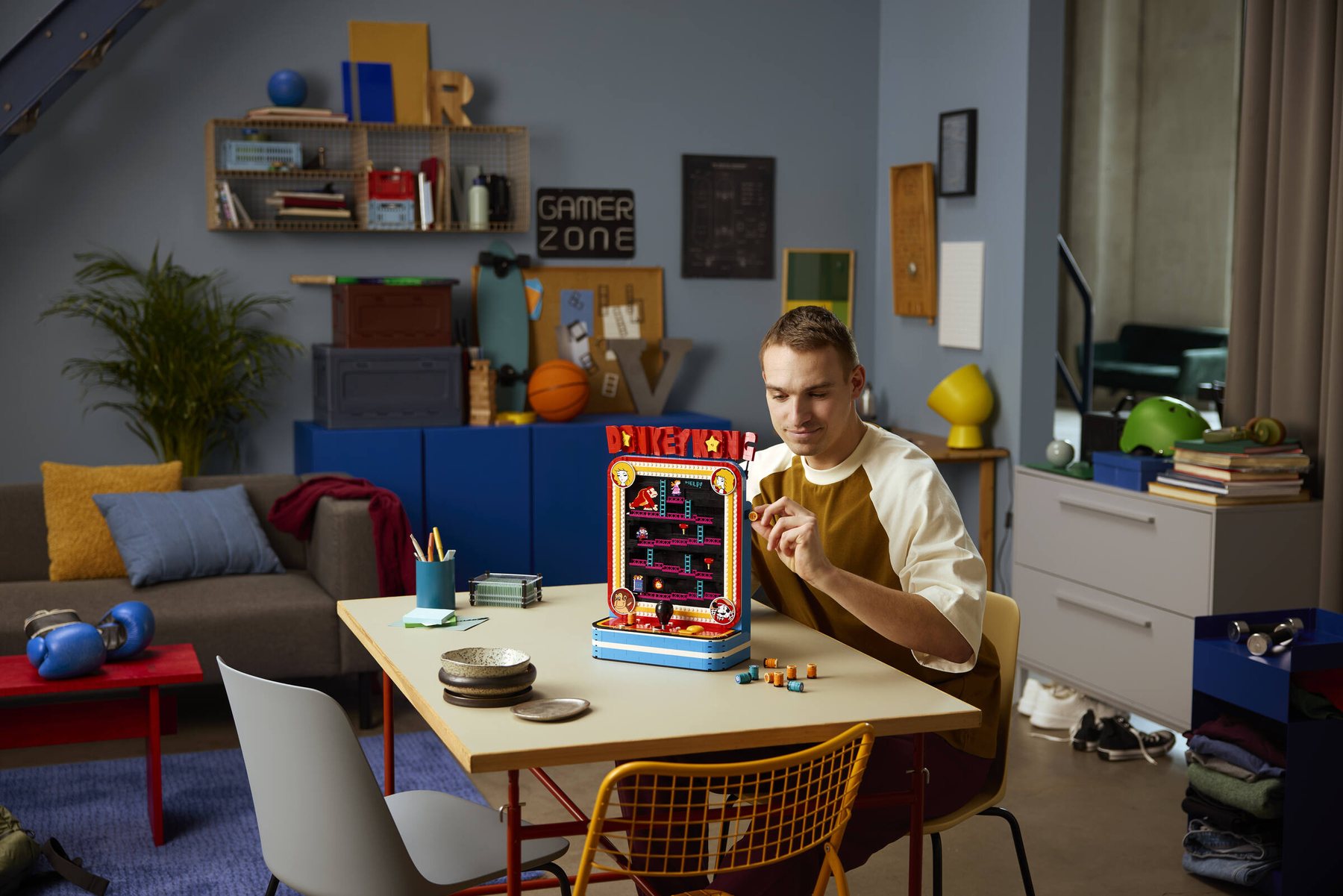 A man sitting at a table, placing a barrel part into the side of an assembled LEGO® Donkey Kong™ Arcade set.